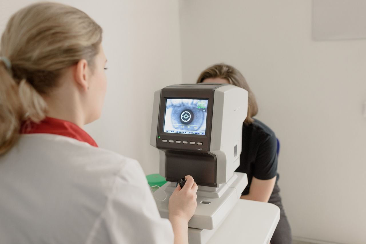 Unrecognizable ophthalmologist checking eyesight of female on vision screener with eye illustration on display in clinic